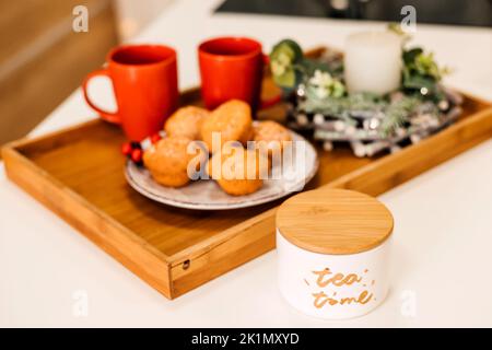 Sul tavolo c'è un piatto di muffin, due tazze rosse e una candela. Anno nuovo Foto Stock