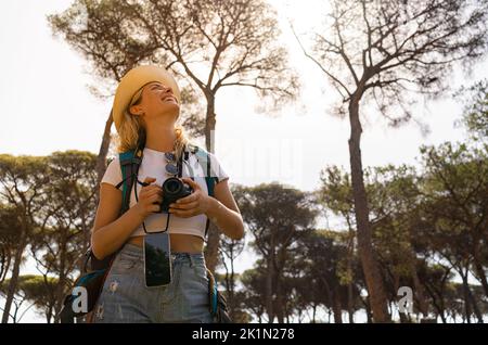Donna intraprendente e felice esplora nella foresta con il suo telefono e la macchina fotografica, donna esploratrice Foto Stock