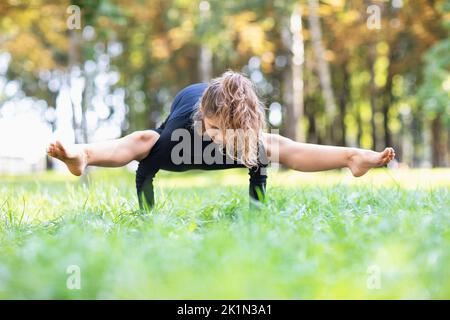 Donna in abbigliamento sportivo nero pratica yoga facendo esercizio titibhasana, posa grasshopper, equilibrio asana sulle mani, esercizio su un caldo morni estivo Foto Stock