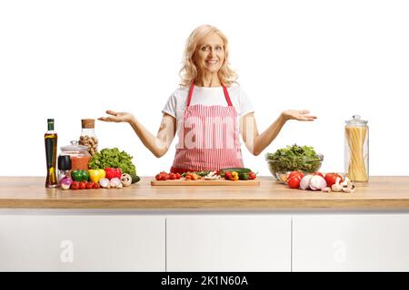 Casalinga con un grembiule in piedi dietro un bancone da cucina con verdure isolate su sfondo bianco Foto Stock