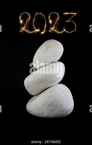 3 pietre bianche impilate, isolate su sfondo nero con 2023 anno nuovo scritto sopra con scintille fuochi d'artificio Foto Stock