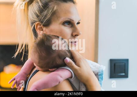 Legame stupefacente fra il bambino del bambino del bambino ed il suo bambino della madre. Ritratto di primo piano interno della donna bionda caucasica che guarda all'infinito mentre tiene stretto il suo neonato accanto al collo. . Foto di alta qualità Foto Stock