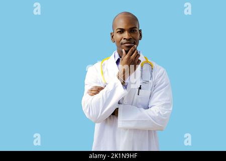 Medico premuroso con braccia ripiegate mano sul mento indossando camice da laboratorio in studio Foto Stock