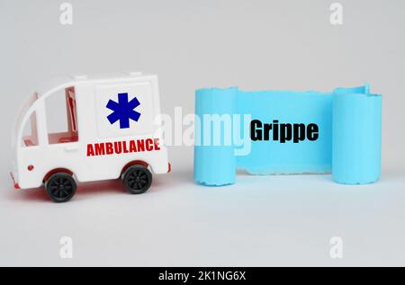 Concetto medico. Su una superficie bianca, un'ambulanza e un cartello di carta blu con l'iscrizione Grippe Foto Stock