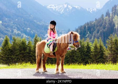 Pony per bambini sulle Alpi. Famiglia primavera vacanza sul ranch cavallo in Austria, Tirolo. I bambini cavalcano i cavalli. Bambino che si prende cura di animali. Foto Stock