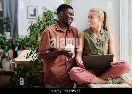 Due giovani e felici manager interculturali che si guardano l'un l'altro durante la discussione dei momenti di lavoro durante l'incontro in ufficio verde Foto Stock