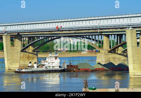 Novosibirsk, Siberia, Russia, 05.18.2022. Ponti sul fiume OB. Una chiatta galleggia sull'acqua sotto il ponte ad arco di ottobre Foto Stock