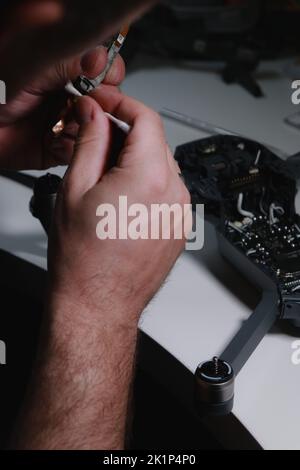 primo piano delle mani di mans riparare un drone su tavolo bianco con diversi attrezzi Foto Stock