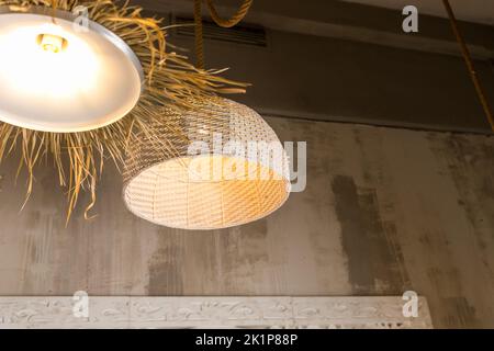 Vista ad angolo basso di due paralumi in vimini e fatti a mano con materiali naturali appesi nel soggiorno. Apparecchiature di illuminazione in stile boho chic. Bambù Foto Stock