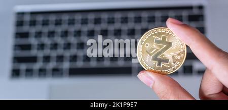 Mano d'affari che tiene Golden Zcash (ZEC) criptovaluta moneta sopra la tastiera del laptop, Crypto è denaro digitale all'interno della rete blockchain, sta usando Foto Stock