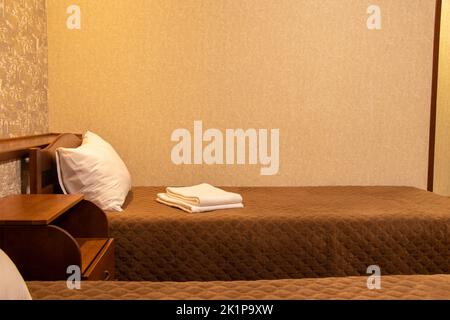 Letto singolo con asciugamani bianchi nella camera da letto nell'edificio dell'appartamento, mobili da camera, letto e plaid marrone Foto Stock