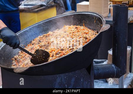 Rinfreschi gratuiti per tutti gli interessati. Street food con steam.Texture di finito gustoso, caldo, nutriente pilaf cottura in stufa di ferro nero per calderone Foto Stock