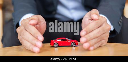 Copertina per uomo d'affari o giocattolo per auto rosso di protezione sul tavolo. Finanziario, denaro, rifinanziamento e concetto di assicurazione auto Foto Stock