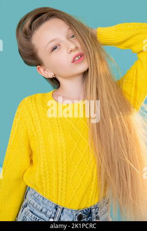 Moda per bambini. Look casual. Collezione autunnale. Ritratto di giovane ragazza dolce fiduciosa modello con lunghi capelli leali in giallo brillante maglione jeans jeans po denim Foto Stock