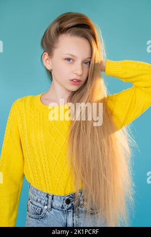 Moda bambino. Stile informale. Collezione autunnale. Ritratto di bella giovane modella ragazza con lunghi capelli leali in jeans maglione giallo posa isolato Foto Stock