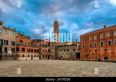 Piccola piazza circondata da tipiche case antiche come campanile su sfondo a Venezia. Foto Stock