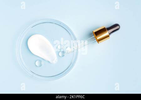 striscio di crema e goccia rotonda trasparente di siero gel in una capsula di petri su sfondo blu. Test di laboratorio di concetto e ricerca, fare e. Foto Stock