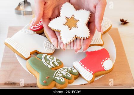 Decorazione festosa panetteria. Pan di zenzero di Natale. Biscotti fatti in casa. Tradizione di Capodanno. Mani femminili irriconoscibili che mostrano la figura decorata festosa i Foto Stock