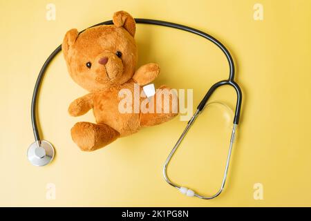 Stetoscopio con bambola Bear su sfondo giallo per sostenere la vita e la malattia dei bambini. Settembre Infanzia mese di consapevolezza del cancro, salute e vita Foto Stock