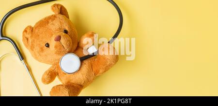 Stetoscopio con bambola Bear su sfondo giallo per sostenere la vita e la malattia dei bambini. Settembre Infanzia mese di consapevolezza del cancro, salute e vita Foto Stock
