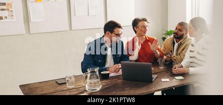 Gruppo di uomini d'affari creativi che hanno una discussione utilizzando un computer portatile in un ufficio moderno. Uomini d'affari diversi che condividono idee mentre lavorano insieme Foto Stock