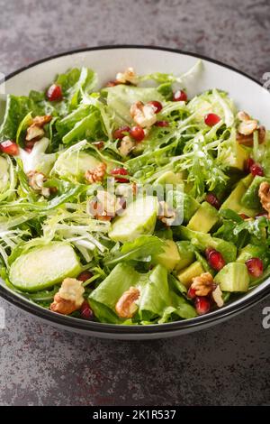 Bruxelles germogli melograno, avocado, noci e lattuga Salad primo piano nella ciotola sul tavolo. Verticale Foto Stock