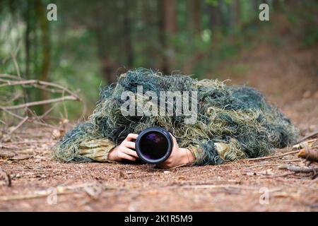 Fotografo che indossa abiti camouflage nella foresta, fotografia di animali selvatici con una macchina fotografica e teleobiettivo Foto Stock