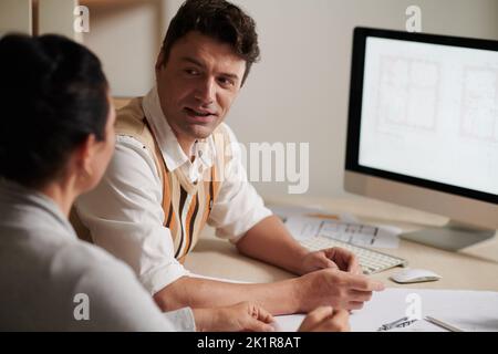 Architetto sorridente e maturo che discute le idee con il collega durante la riunione Foto Stock
