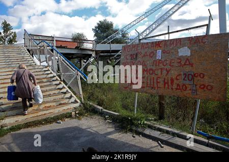 IZIUM, UCRAINA - 19 SETTEMBRE 2022 - Una donna trasporta le borse sulle scale di un ponte pedonale danneggiato come un bordo ha informazioni circa le ore di Foto Stock