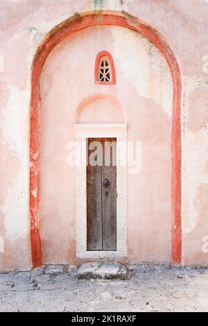Un'immagine verticale di una porta in legno di un edificio con pareti rosa con belle sculture in cima Foto Stock