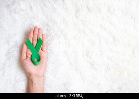 Mano che tiene nastro verde per sostenere la gente che vive e la malattia. Fegato, cistifelline dotto biliare, cancro al rene e linfoma consapevolezza del mese concetto Foto Stock