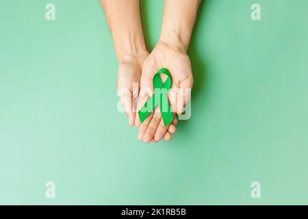 Mano che tiene nastro verde per sostenere la gente che vive e la malattia. Fegato, cistifelline dotto biliare, cancro al rene e linfoma consapevolezza del mese concetto Foto Stock