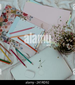 Una foto sopra la testa di una scrivania con un MacBook, airpod, sketchbook e matite Foto Stock