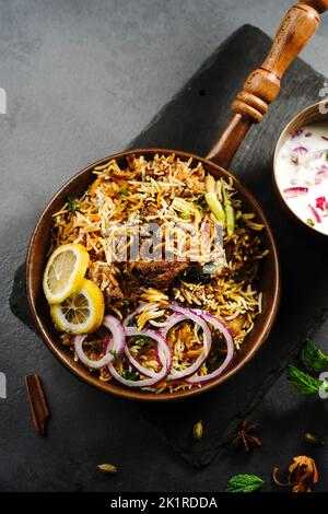 Hyderabadi Mutton capra biryani servito con yogurt raita in ambiente moody Foto Stock