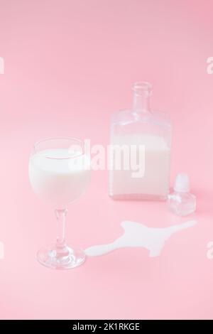 bicchiere con latte e un grafico sullo sfondo. sfondo rosa. budino di latte versato Foto Stock