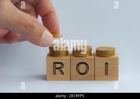 Mettere a mano monete su blocchi di legno con testo ROI inciso su cubi di legno - Business and Investment Concept. Foto Stock