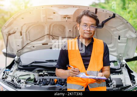 maschio in piedi uniforme di sicurezza con check list in auto cofano anteriore aperto. reclamo regolatore ingegnere meccanico uomo ritratto felice. Foto Stock