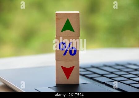 Blocco di legno a forma di cubo sulla tastiera del computer portatile con icona percentuale e simbolo freccia su e giù. Concetto di fluttuazione degli affari e degli interessi. Foto Stock