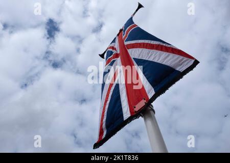 Bandiera nazionale britannica come una bandiera su un palo che sbatte nel vento contro un cielo nuvoloso. Piano sullo sfondo Foto Stock