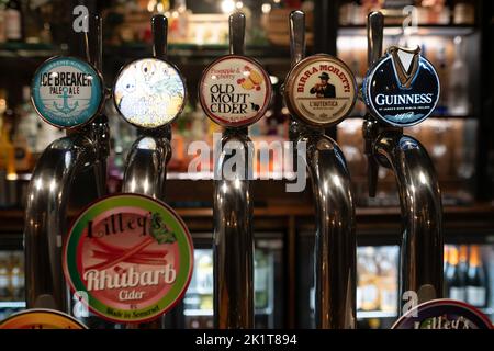 Birre alla spina in acciaio inossidabile in un pub inglese con diversi tipi e marche di birre e bevande. Profondità di campo ridotta Foto Stock