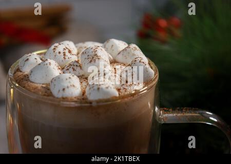 primo piano di mini marshmallows sulla cioccolata calda in una tazza di vetro, sfondo sfocato luci Foto Stock