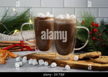 cioccolata calda in tazze di vetro con mini marshmallows sul tavolo grigio, sfondo di natale sfocato Foto Stock