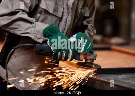 Primo piano di un maschio irriconoscibile che taglia il metallo con l'attrezzo elettrico in officina, scintille che volano, spazio di copia Foto Stock