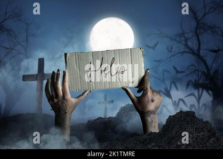 Mani di zombie che tengono il cartone con il testo DI AIUTO mentre uscendo dalla tomba di notte Foto Stock