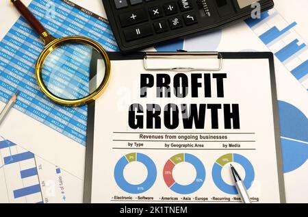Concetto aziendale. Sullo sfondo di grafici e grafici, ci sono articoli per ufficio e una tavoletta con documenti e l'iscrizione - LA CRESCITA DEL PROFITTO Foto Stock