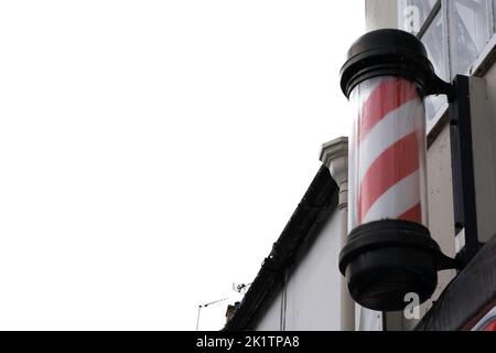 Barber's pole attaccata alla parete sopra un barbiere a Chipping Norton, Regno Unito, su sfondo bianco Foto Stock