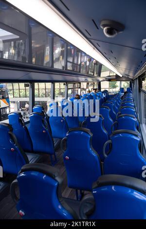 Interno del ponte superiore in un moderno autobus a due piani con posti a sedere blu. Ci sono alcuni passeggeri nella parte anteriore. Concentrarsi sulla parte anteriore dell'autobus Foto Stock