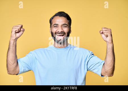 Felice eccitato indiano uomo alzando pugni isolati su sfondo giallo. Foto Stock