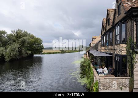 Il fiume Great Ouse si snoda tra prati nel villaggio storico di St Ives, Cambridgeshire. Sulla destra ci sono case e persone in un ristorante Foto Stock
