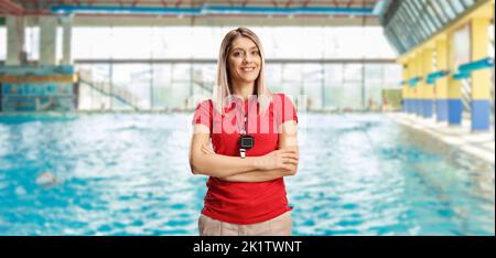 Allenatore di nuoto femminile con un wistle e cronometro intorno al collo che si posa su una piscina interna Foto Stock